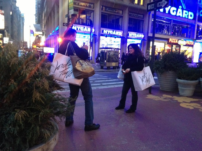 A pair of NYC tourists near Times Square taking the obligatory picture in the middle of the street/sidewalk. They, thankfully, aren't in the way of a bunch of foot traffic.